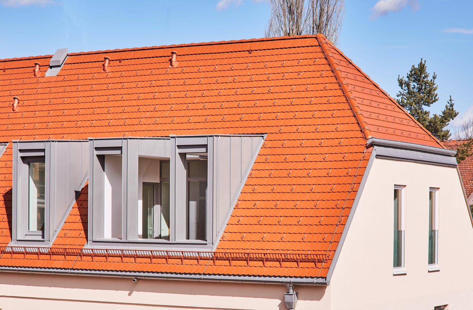 Detailansicht eines Daches mit roten Ziegeln und modernen Dachgauben.