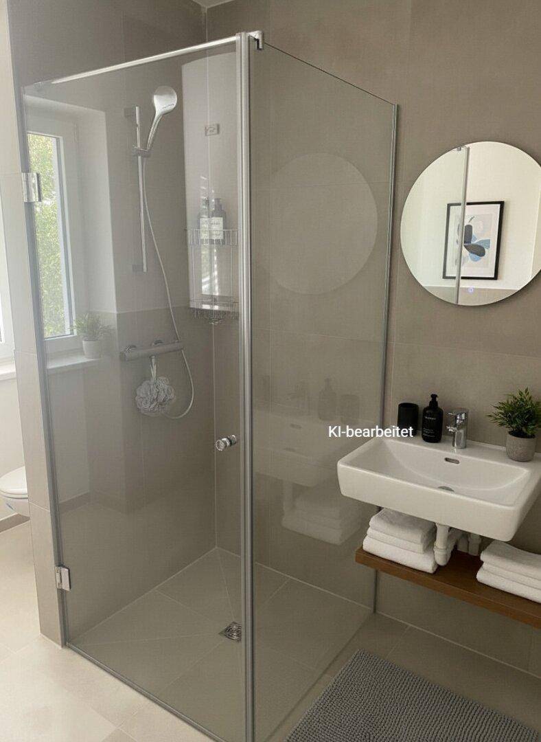Modernes Badezimmer mit begehbarer Dusche, Waschbecken, rundem Spiegel und einem Fenster.