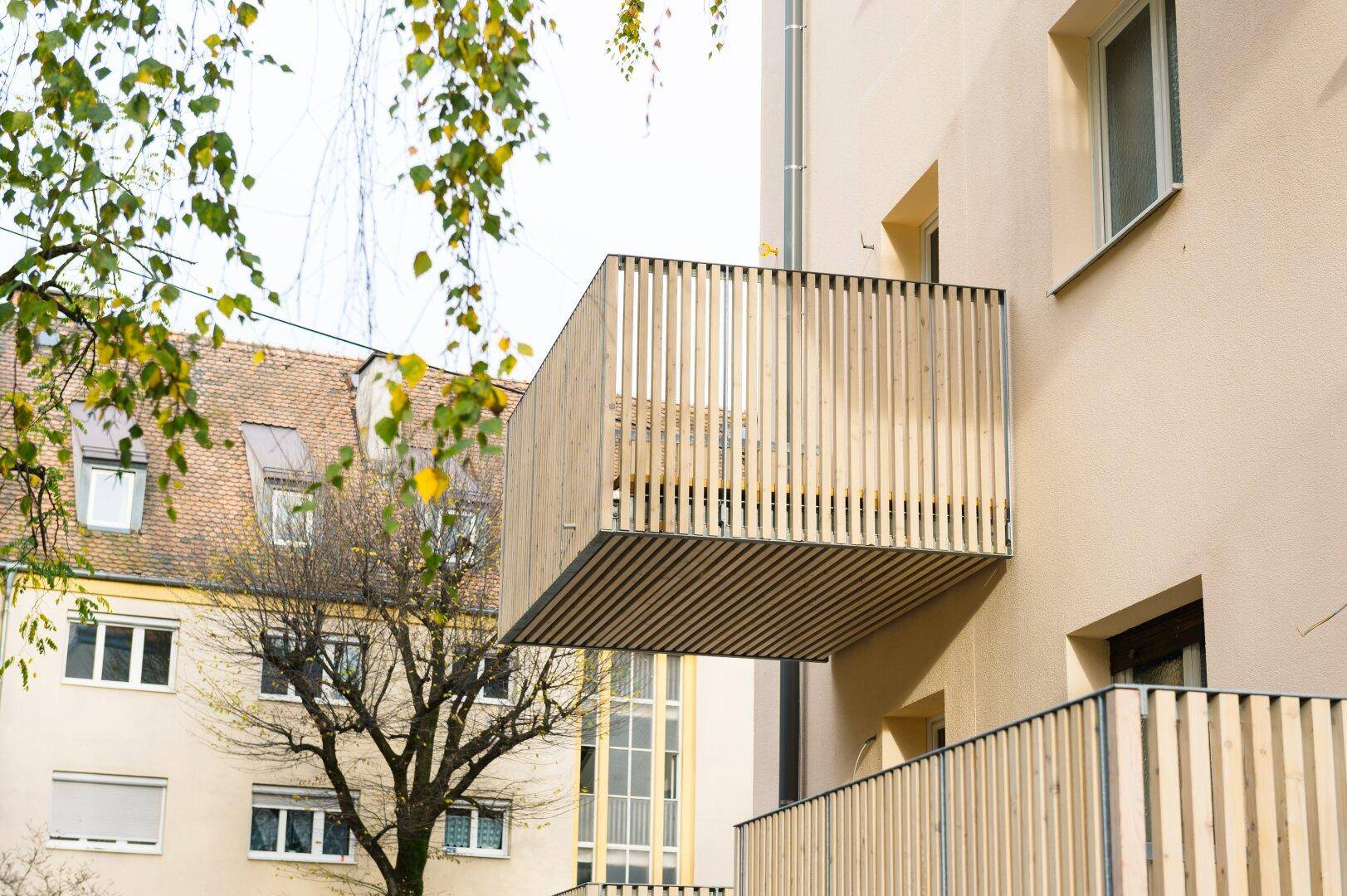 Moderner Holzbalkon an einem Mehrfamilienhaus mit vertikalen Lamellen und Blick auf die Umgebung.