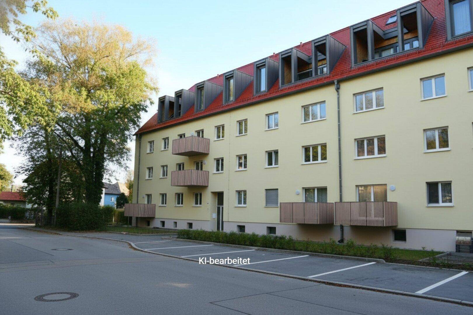 Mehrfamilienhaus mit Balkonen und Parkplätzen im Vordergrund, unter einem klaren Himmel.