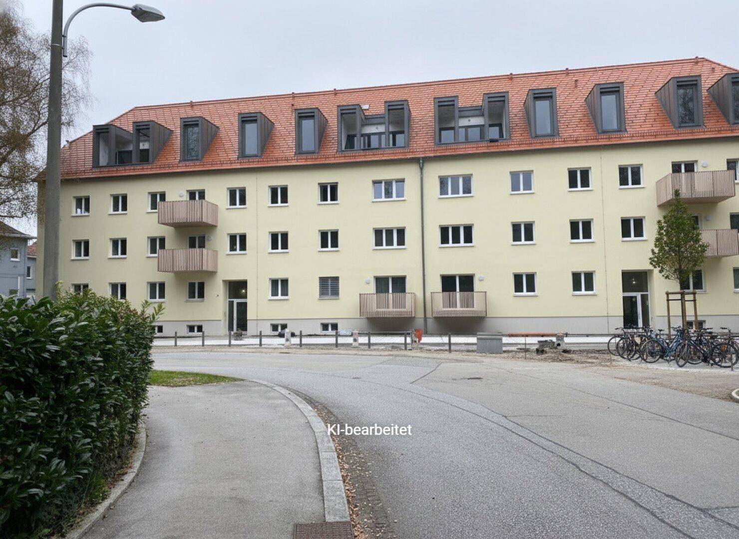 Ansicht eines Mehrfamilienhauses von der Straße mit Balkonen und Fahrradstellplätzen.