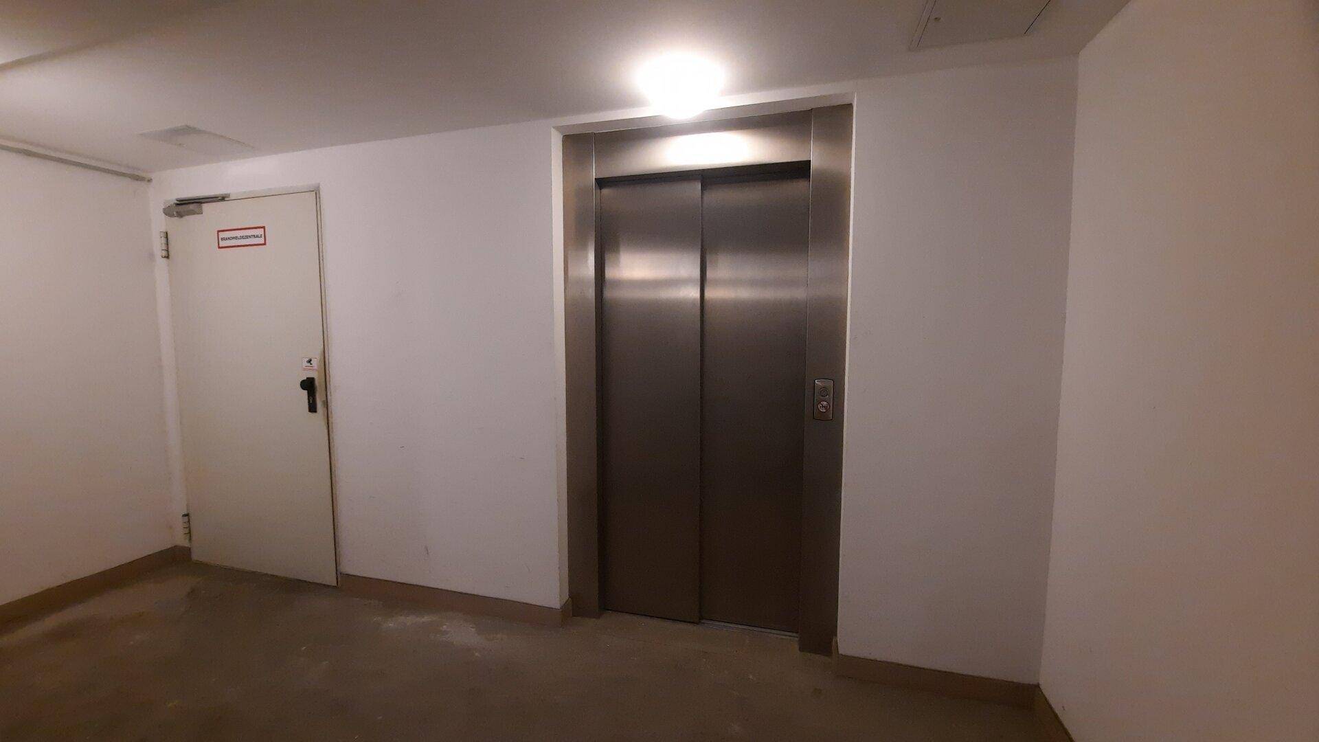 Heller Flur mit einer modernen Edelstahllift-Tür und einer weiteren weißen Tür.