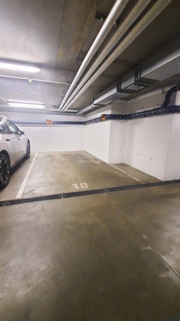 Detailansicht eines Parkplatzes Nummer 10 in der Tiefgarage mit Betonboden und Deckeninstallationen.