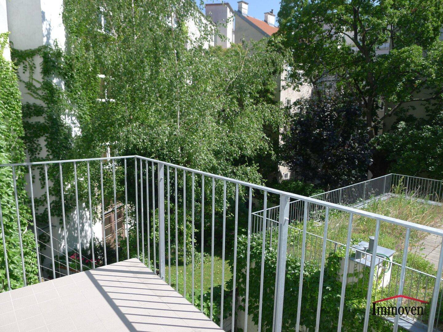 Balkon mit Blick auf einen grünen Innenhof mit Bäumen und bewachsenen Wänden.