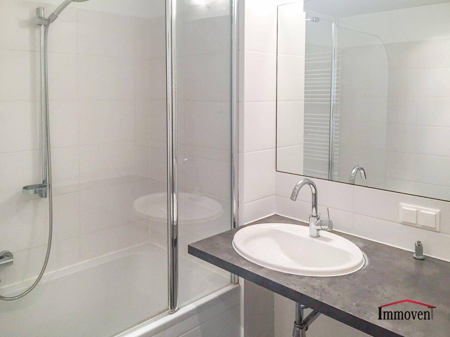 Helles Badezimmer mit Badewanne, Duschabtrennung aus Glas und großem Spiegel über dem Waschtisch.