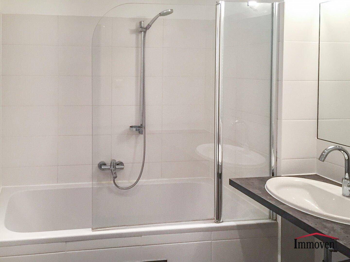 Modernes Badezimmer mit Badewanne, Duschfunktion und Waschtisch mit dunkler Ablage.