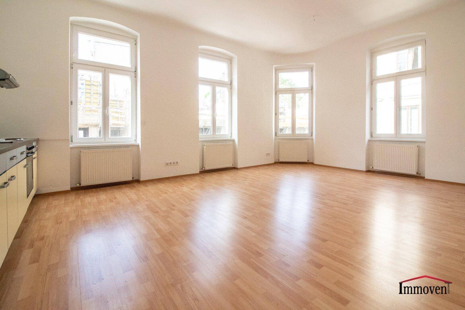 Geräumiger Wohnbereich mit hellem Parkettboden und mehreren großen Fenstern für viel natürliches Licht.