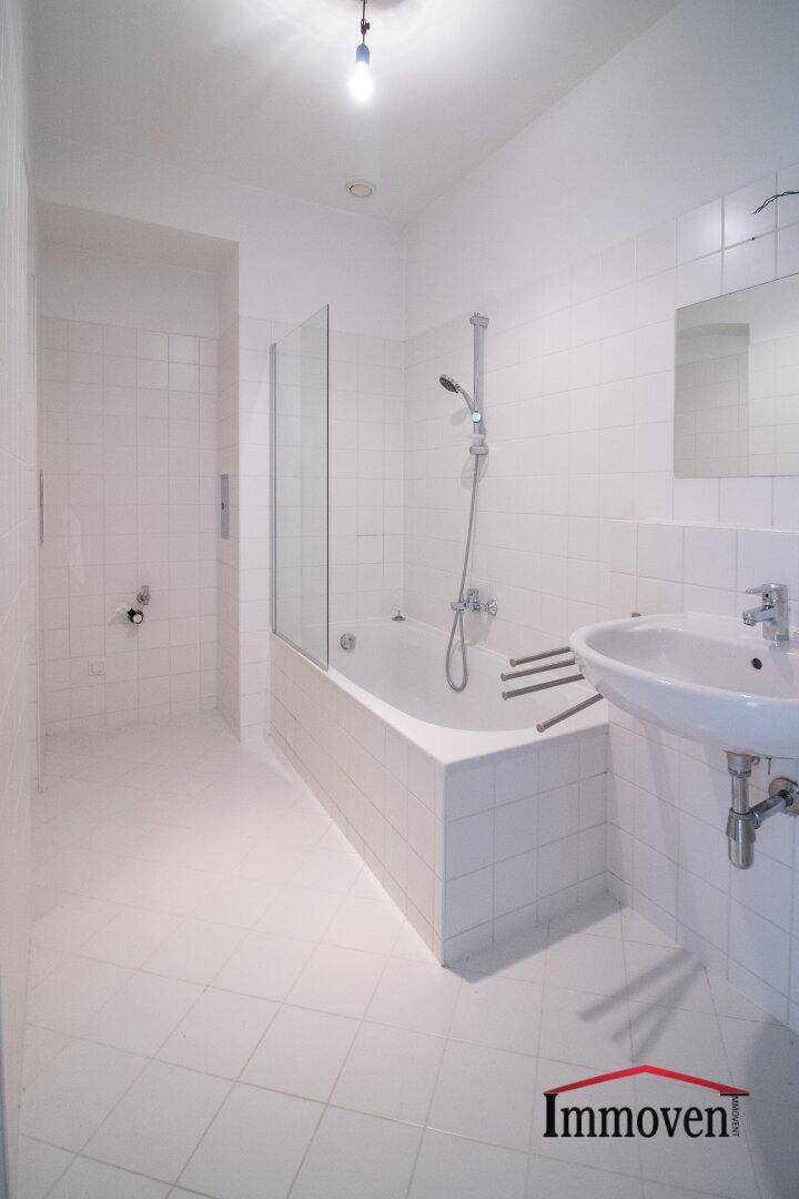 Helles Badezimmer mit weißen Fliesen, Badewanne mit Duschfunktion und einem Waschbecken.