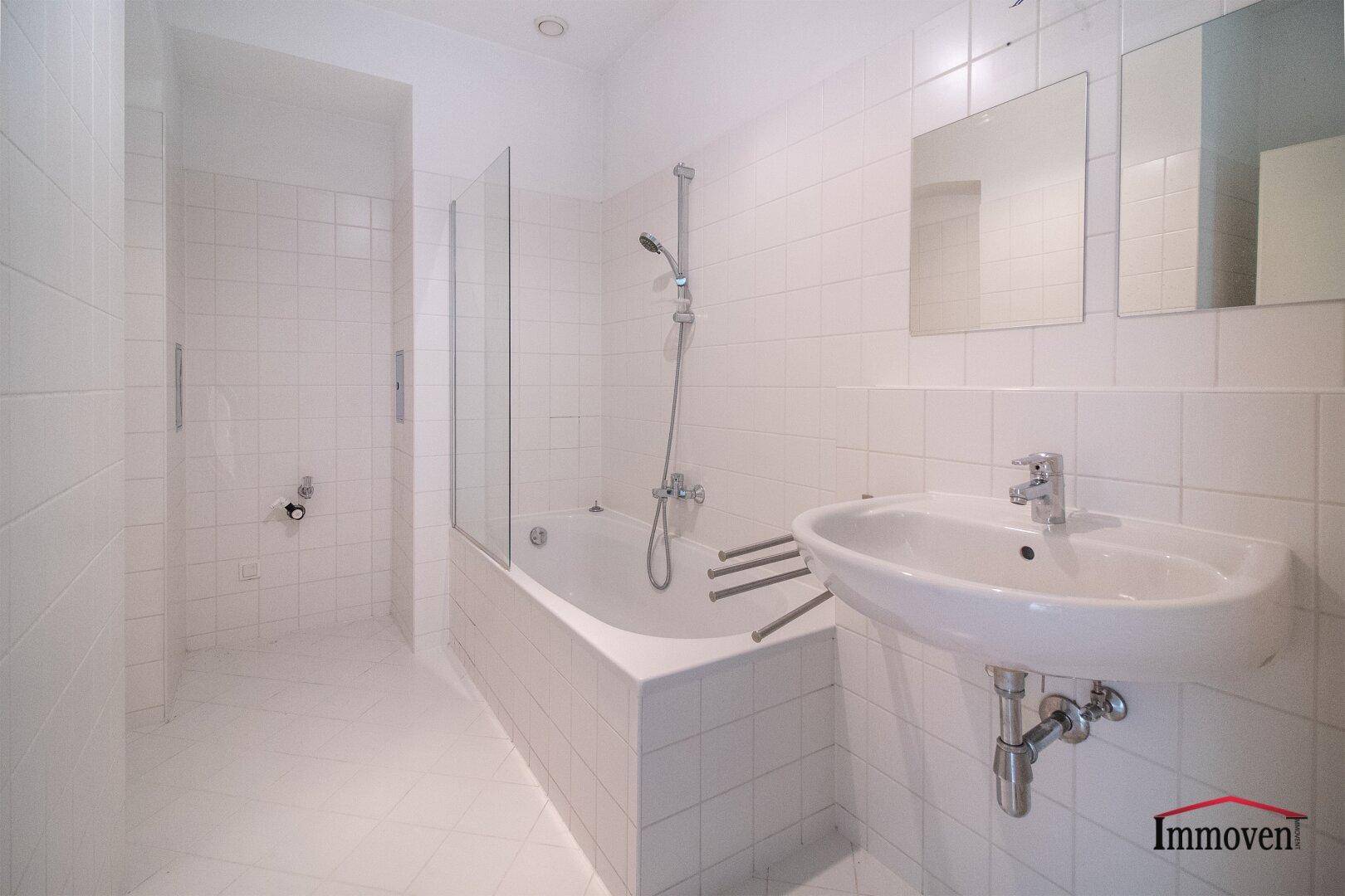 Weiß gefliestes Badezimmer mit Badewanne, Duscharmatur und einem modernen Waschbecken.
