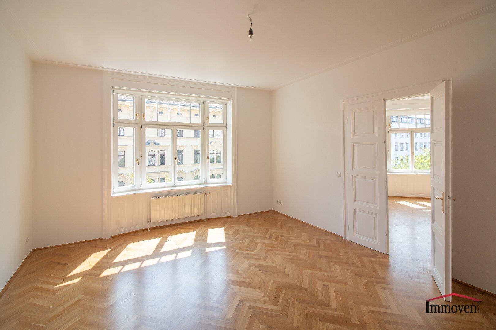 Lichtdurchfluteter Wohnraum mit klassischem Fischgrätparkett und einem breiten Fenster mit Blick nach draußen.