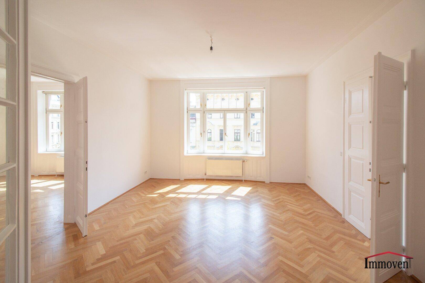 Heller Wohnraum mit Fischgrätparkett und großen Fenstern, die viel Tageslicht hereinlassen.