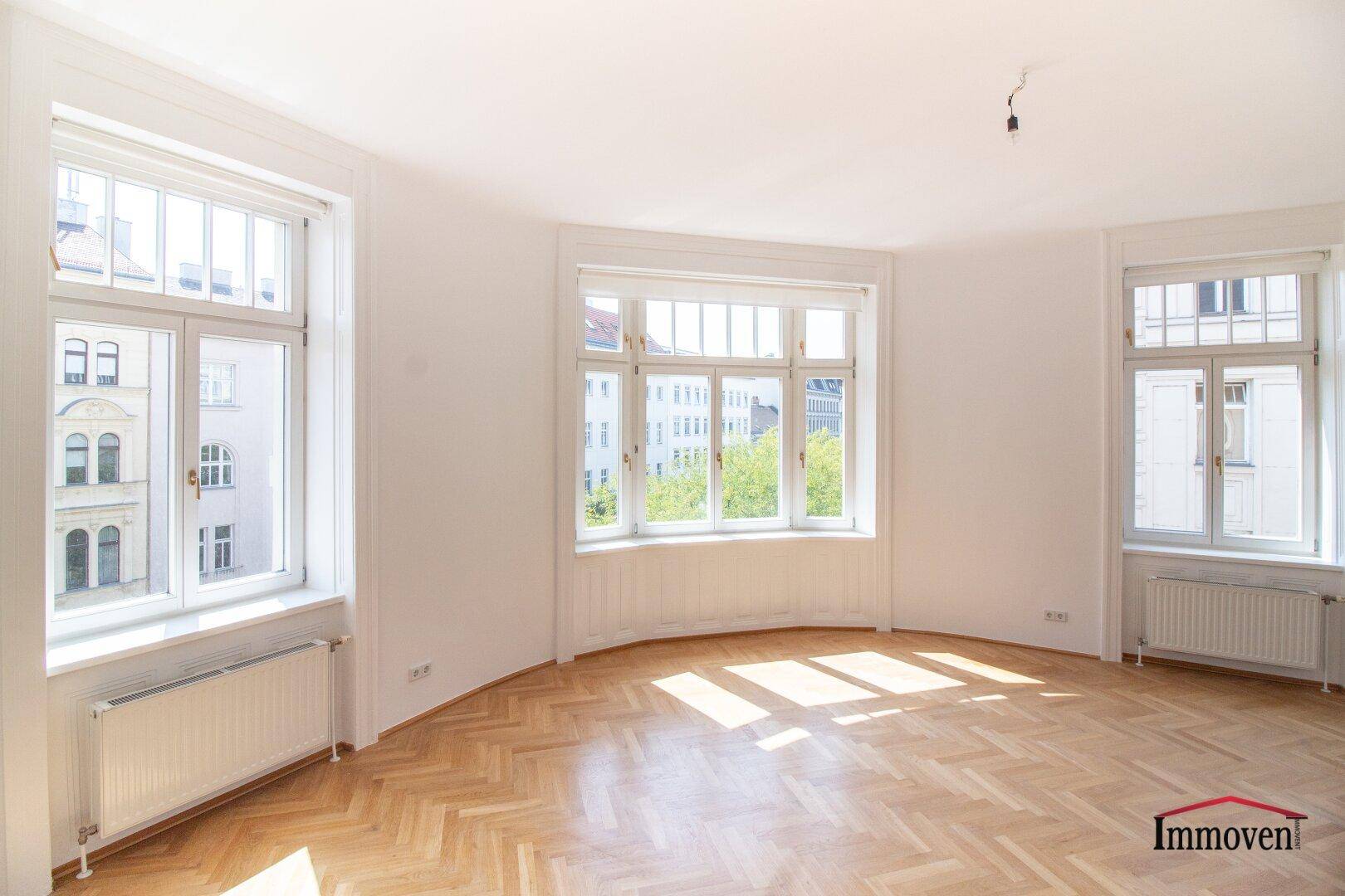 Heller Wohnbereich mit Fischgrätparkett und einer Reihe von Fenstern, die den Raum mit Licht füllen.