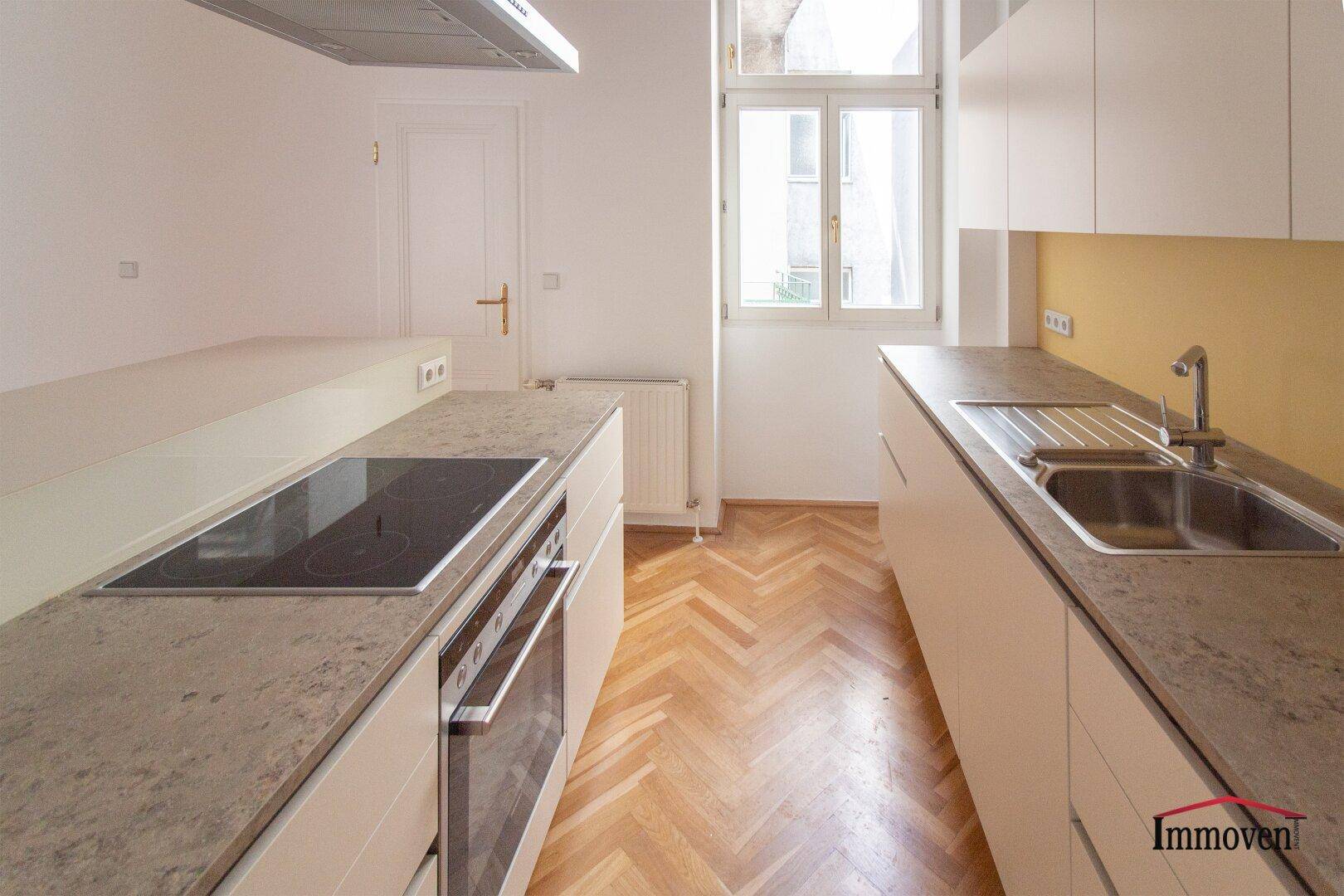 Küchenzeile mit Spüle, Arbeitsplatte und Induktionskochfeld, daneben ein Fenster mit Blick nach draußen.