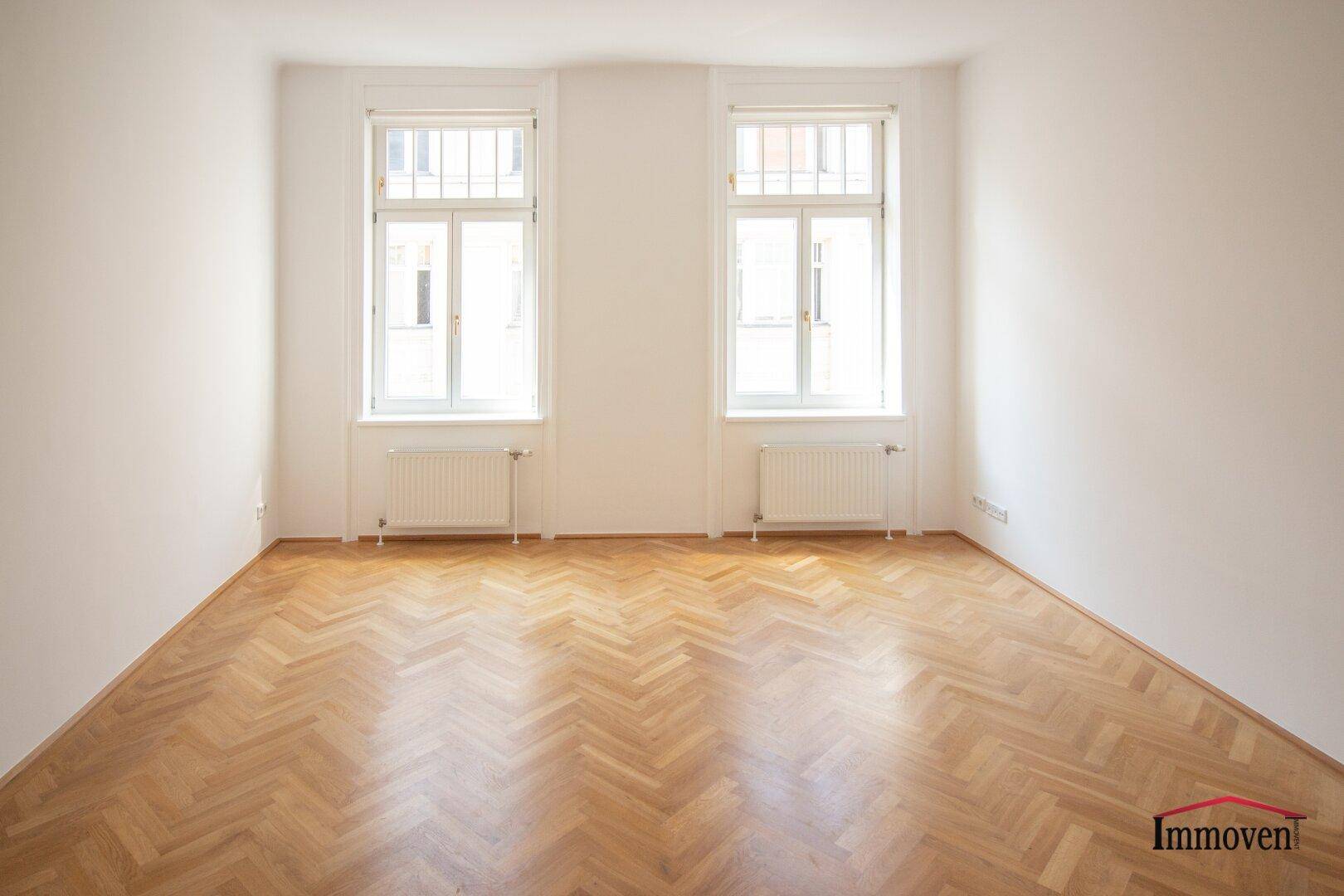 Helles Schlafzimmer mit zwei Fenstern und Fischgrätparkett, bietet eine ruhige Atmosphäre.