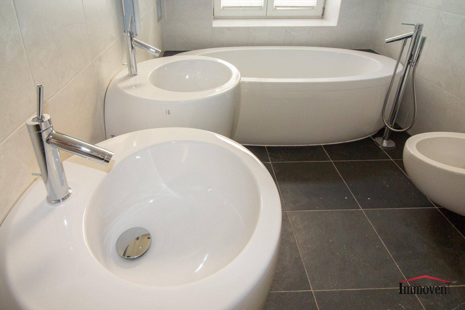 Nahaufnahme von zwei modernen Waschbecken und einer Badewanne in einem gefliesten Badezimmer.