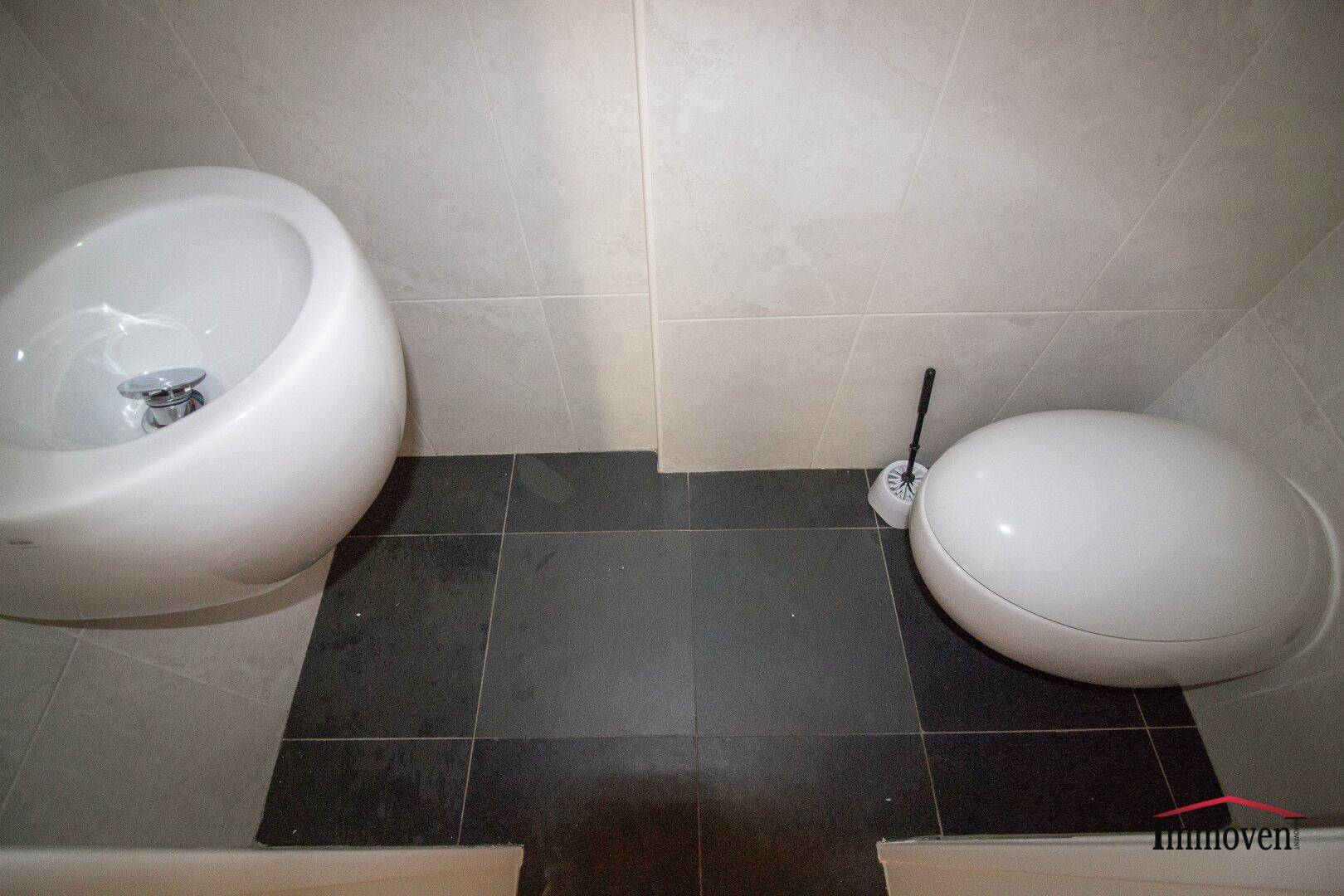 Modernes Gäste-WC mit runden Sanitärobjekten und kontrastierenden Fliesen in Grau.