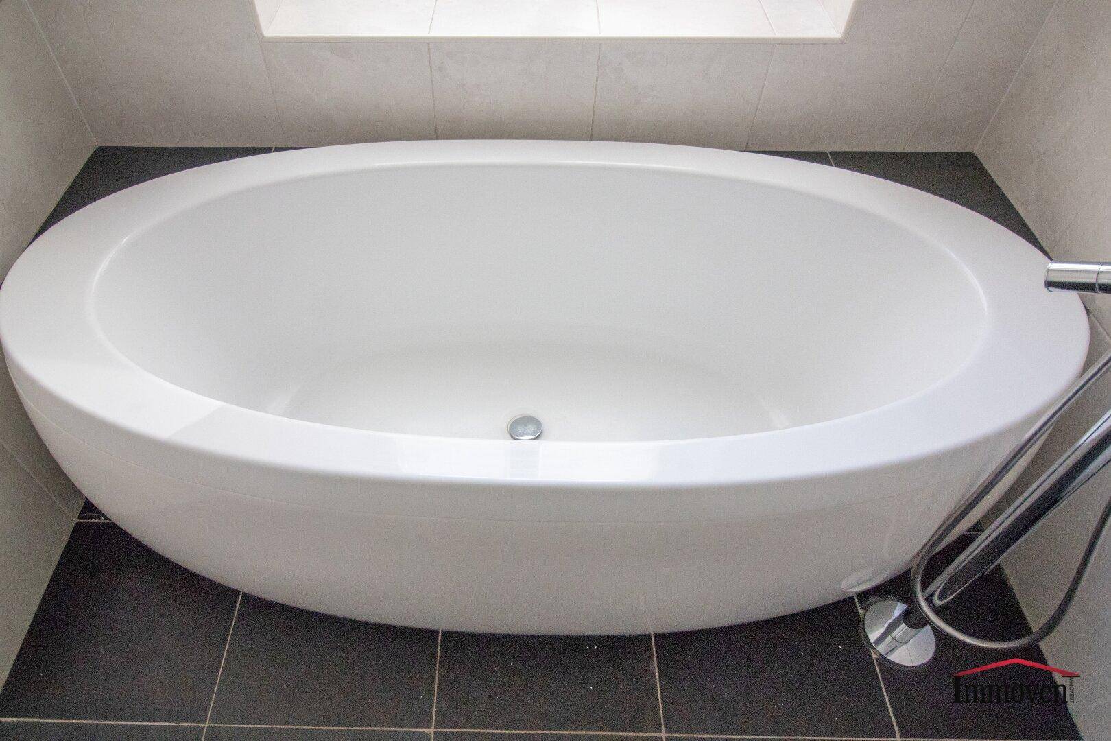 Freistehende ovale Badewanne auf dunklen Fliesen in einem modernen Badezimmer.