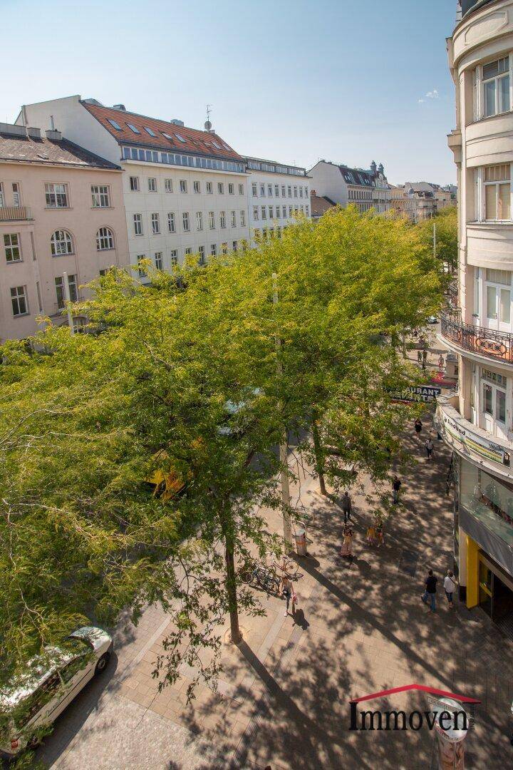 Eine belebte Stadtstraße mit vielen Bäumen und historischen Fassaden unter blauem Himmel.