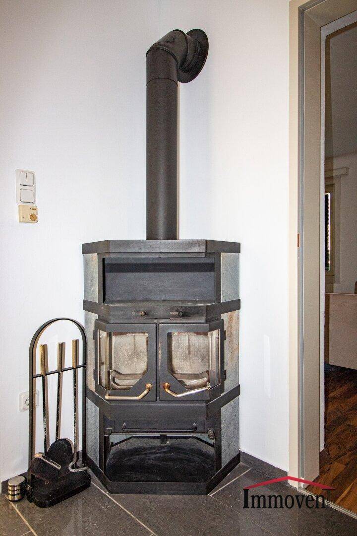 Detailaufnahme eines modernen Kaminofens mit Holzscheiten und Kaminbesteck.