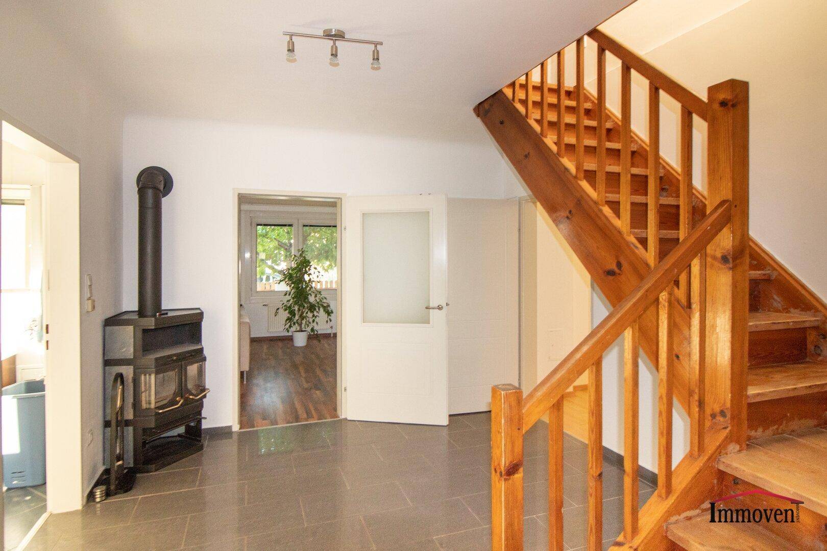 Heller Flur mit Holztreppe, Kaminofen und Fliesenboden.