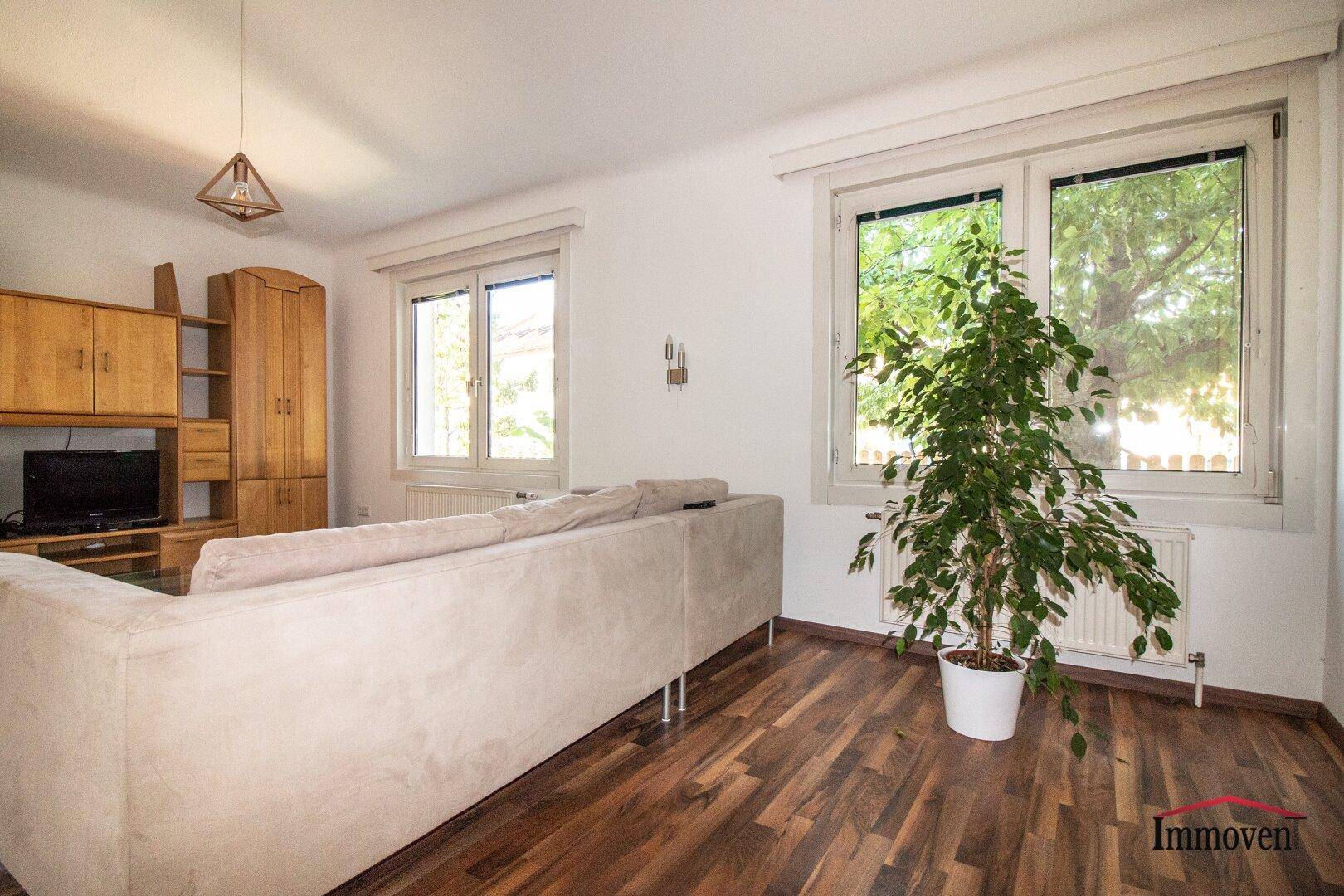 Gemütliches Wohnzimmer mit Holzboden, großem Sofa und Blick ins Grüne.