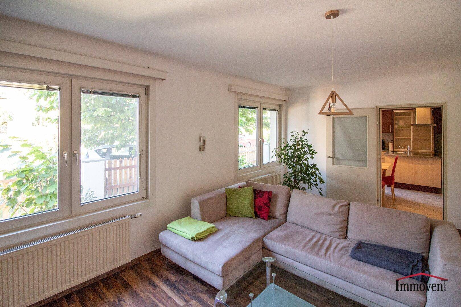 Helles Wohnzimmer mit Sofa, Holzboden und Zugang zu einem weiteren Raum.