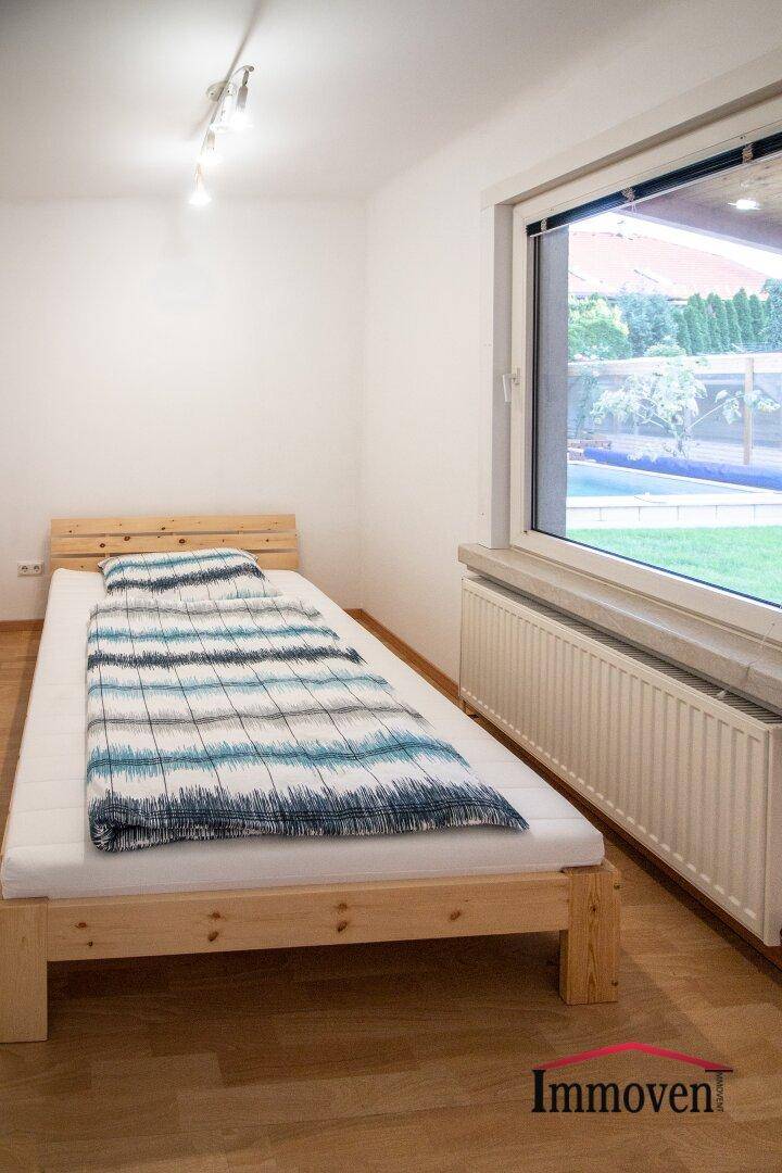 Helles Schlafzimmer mit Holzbett, Holzboden und Blick in den Garten.