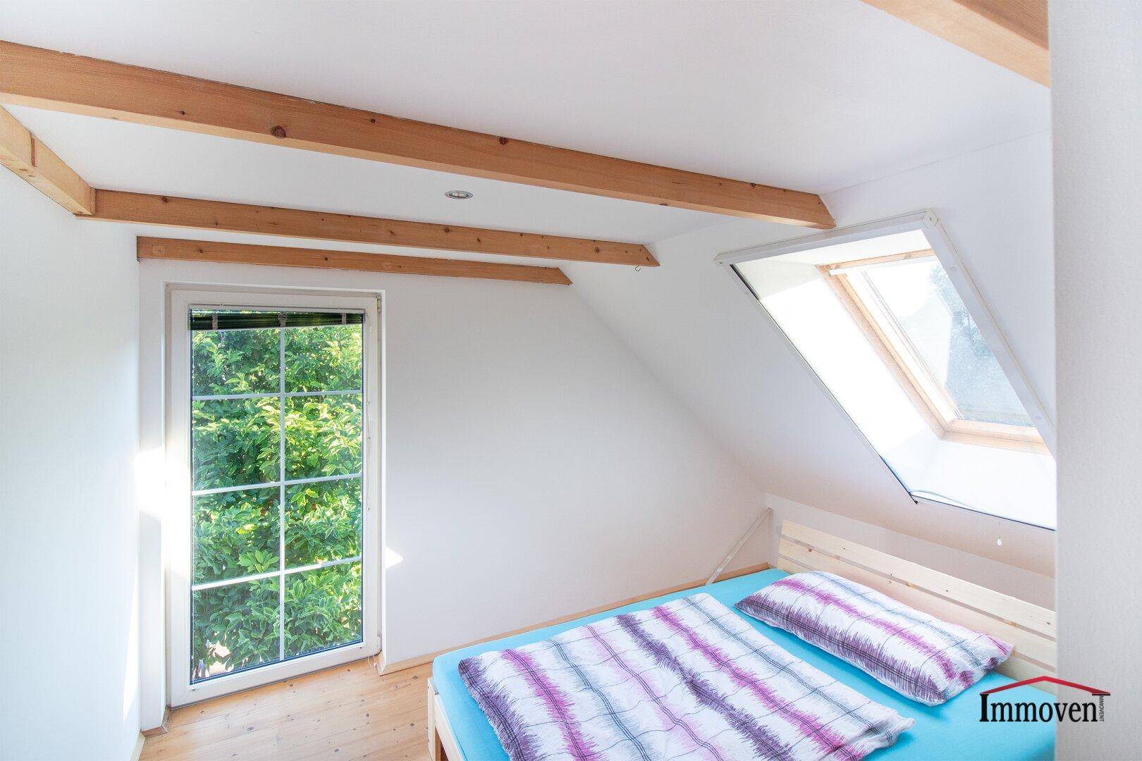 Gemütliches Schlafzimmer im Dachgeschoss mit Holzbalken und Dachfenster.