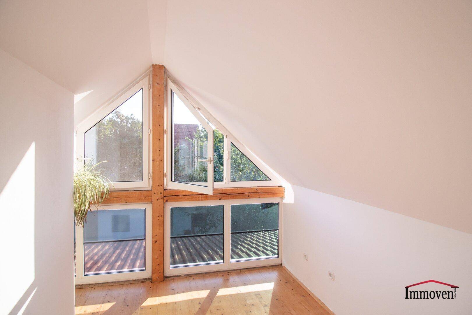 Lichtdurchfluteter Raum im Dachgeschoss mit großen Fenstern und Holzbalken.