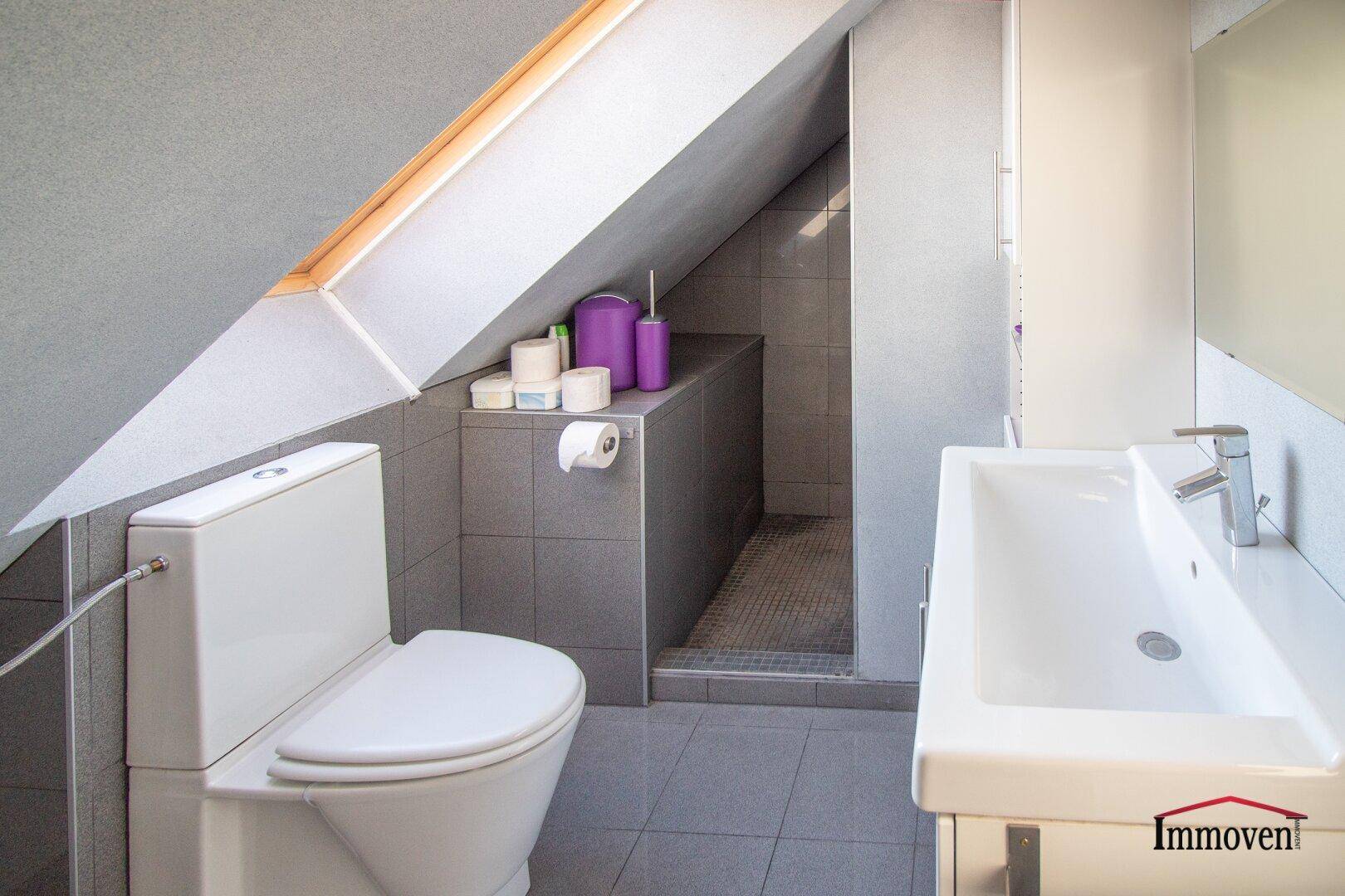 Modernes Badezimmer im Dachgeschoss mit Schräge, WC, Waschbecken und Dusche.