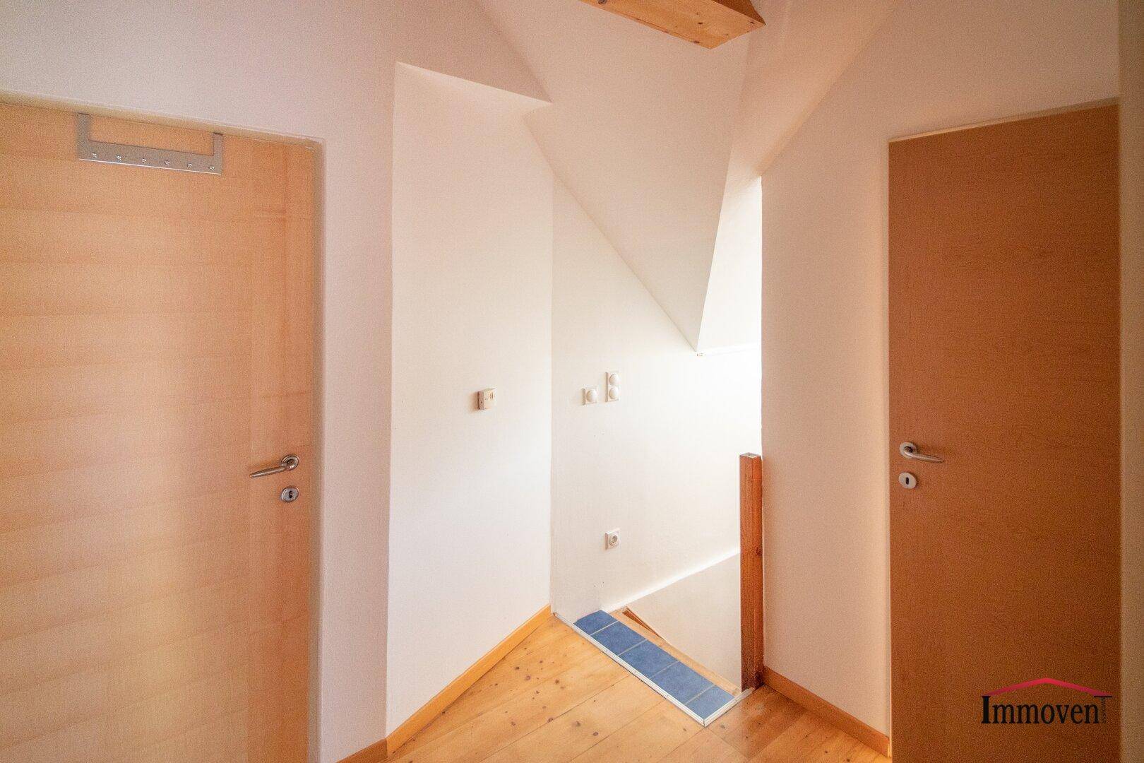 Heller Flur mit Holzfußboden und Treppenaufgang im Dachgeschoss.