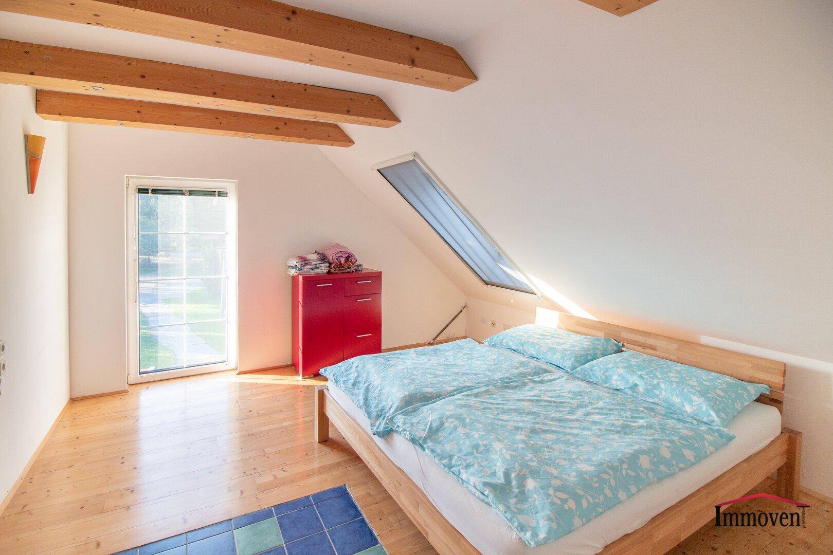 Gemütliches Schlafzimmer im Dachgeschoss mit Holzbalken, Holzbett und Dachfenster.