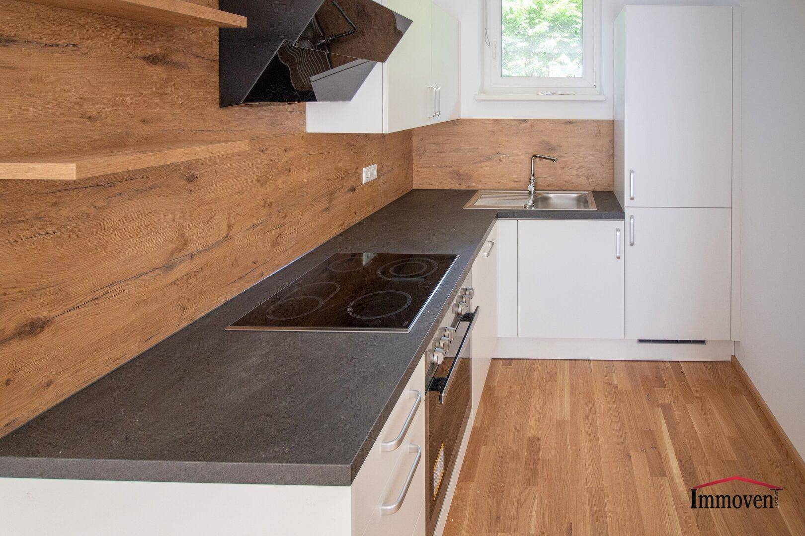 Moderne Einbauküche mit dunkler Arbeitsplatte, Holzrückwand und integriertem Kochfeld.