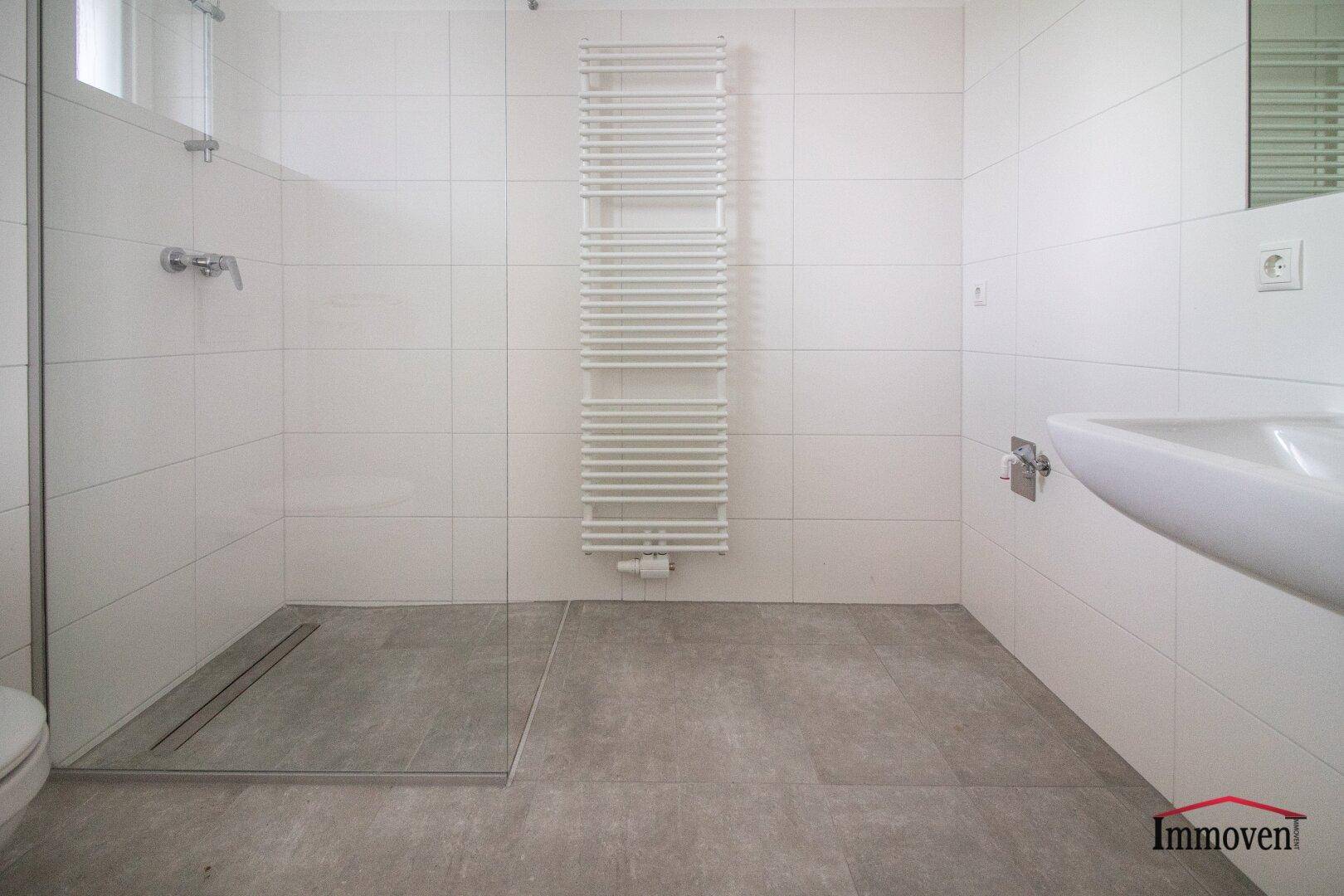 Modernes Badezimmer mit ebenerdiger Dusche, weißen Fliesen und Handtuchheizkörper.