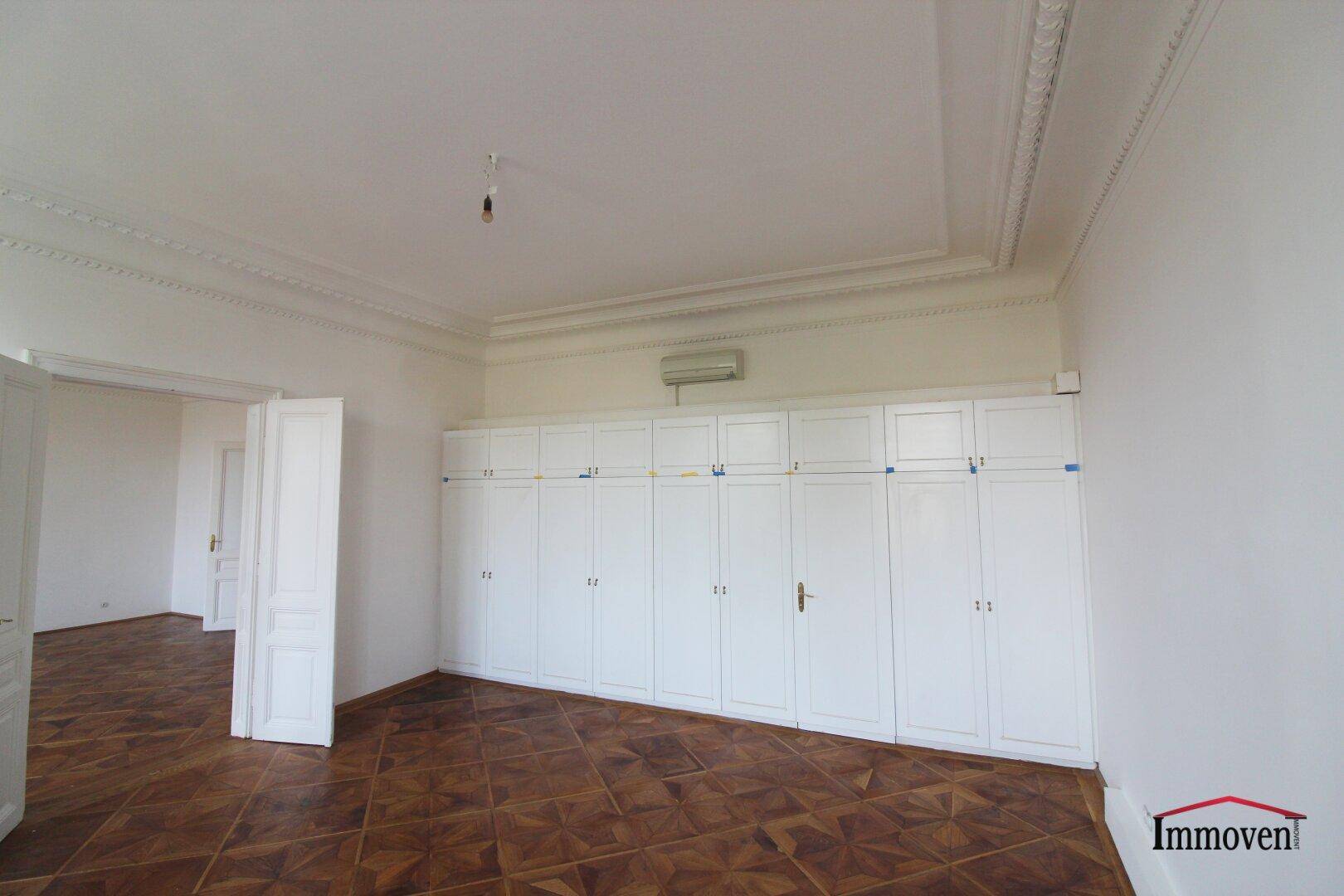Geräumiges Zimmer mit Parkettboden, Einbauschränken und einer Klimaanlage über den Schränken.