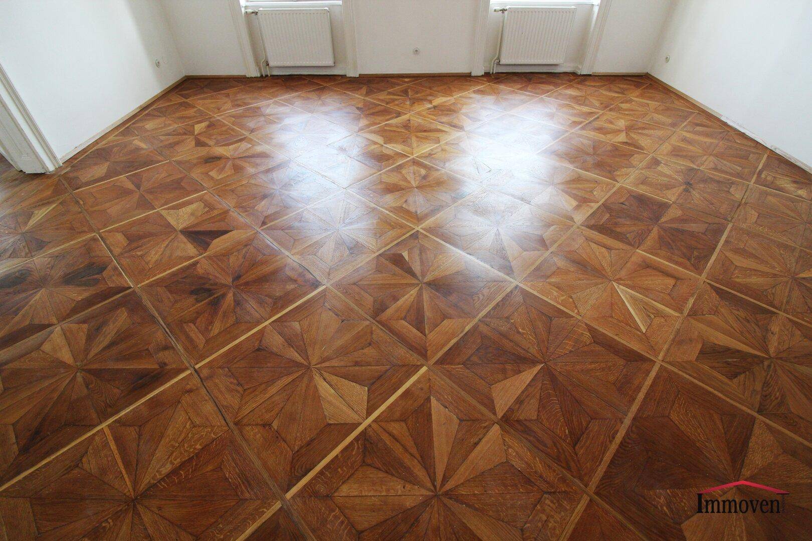 Detailaufnahme eines kunstvoll verlegten Parkettbodens mit geometrischem Muster in einem hellen Raum.
