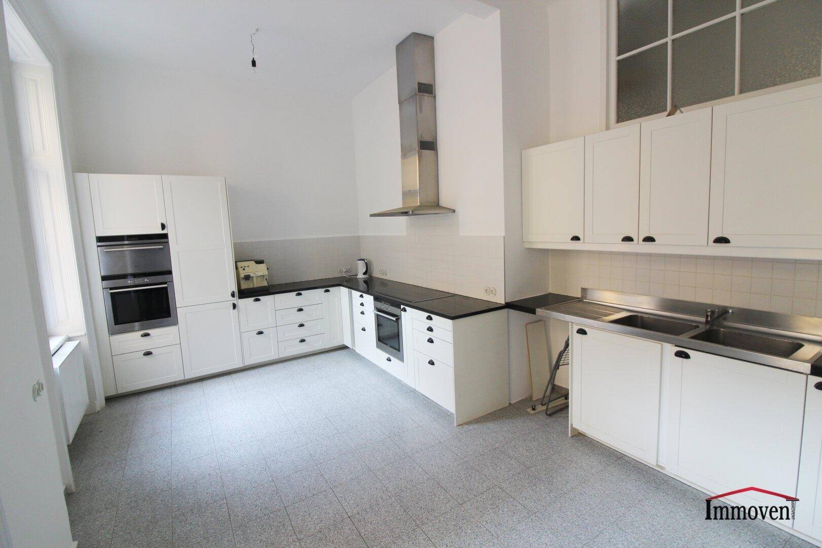 Moderne Einbauküche mit weißen Schränken, dunklen Arbeitsplatten und Edelstahlgeräten. Ein großes Fenster sorgt für Helligkeit.