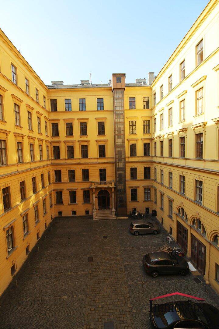 Blick auf einen sonnigen Innenhof eines Altbaus mit gepflastertem Bereich und einem modernen Aufzug.
