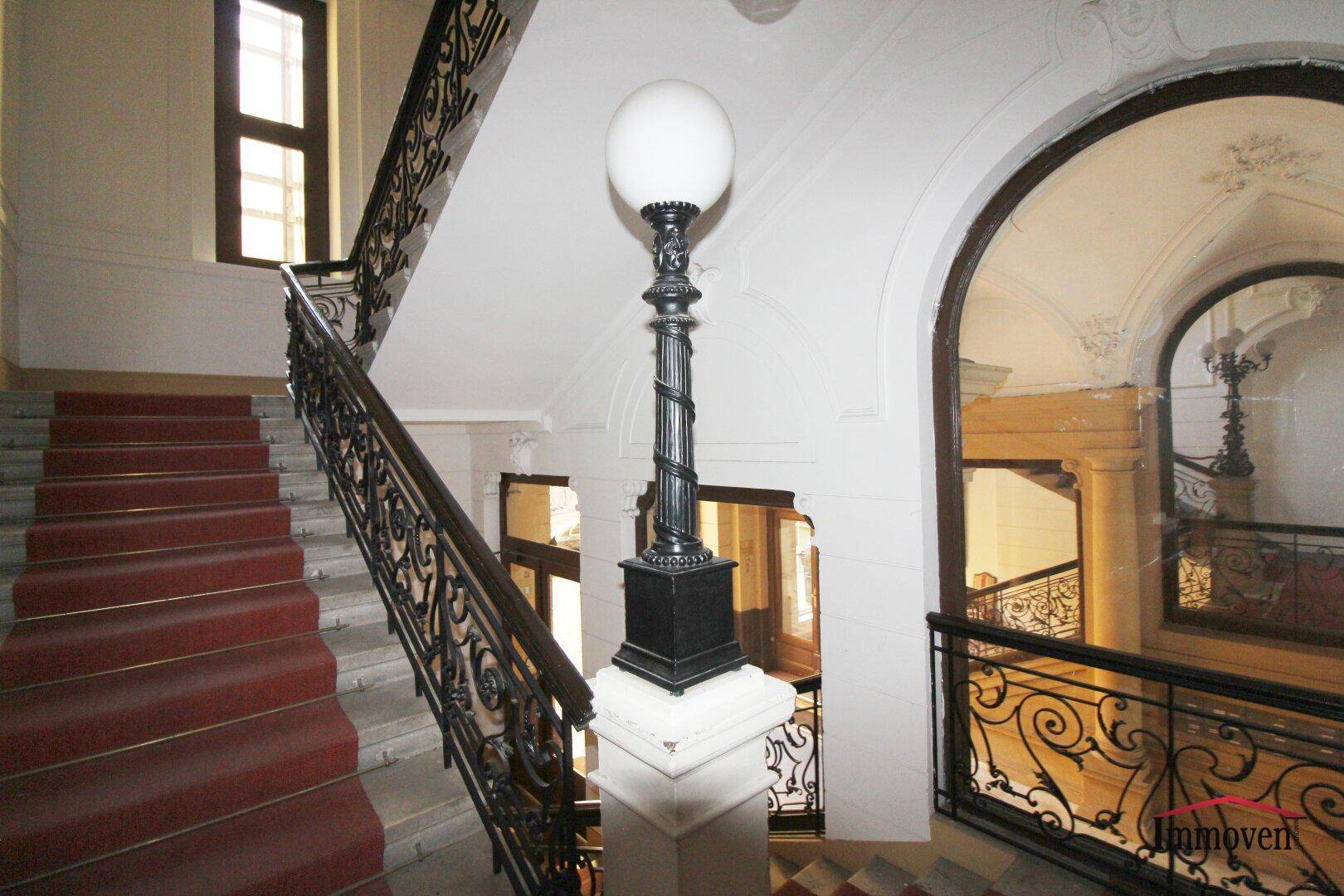 Elegantes Treppenhaus mit rotem Teppich, schmiedeeisernem Geländer und einem historischen Treppenpfosten.