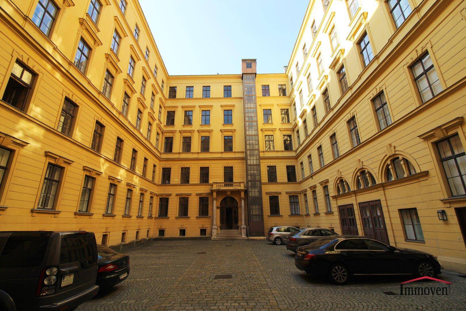 Innenhof eines historischen Gebäudes mit gepflastertem Boden, parkenden Autos und einem modernen Aufzug.