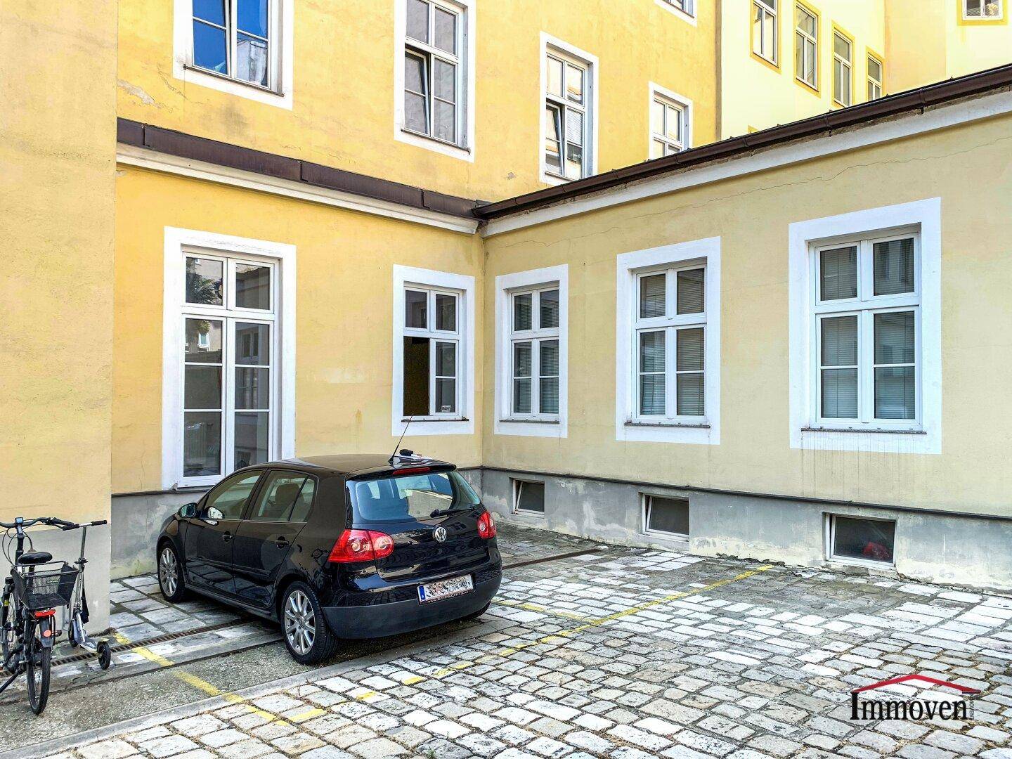 Innenhof eines Gebäudes mit einem geparkten Auto, Fahrrad und Kopfsteinpflaster.