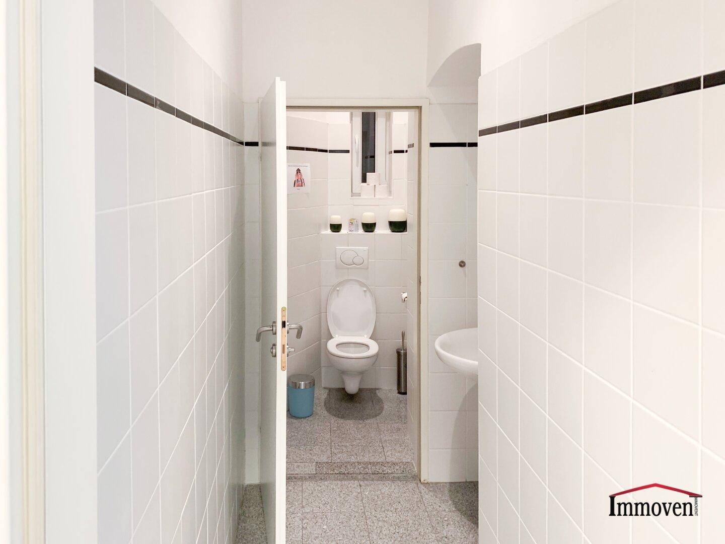 Sauberer Toilettenraum mit weißen Fliesen, einer Toilette und einem Waschbecken.