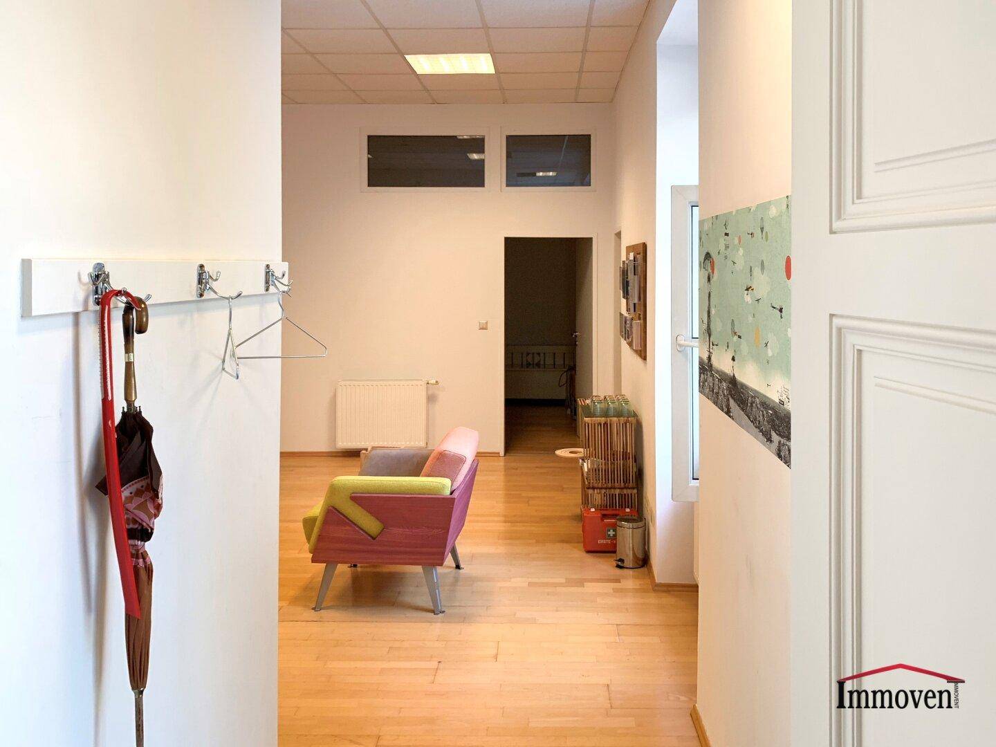 Heller Flur mit Garderobe und Blick auf einen farbenfroh eingerichteten Wartebereich.