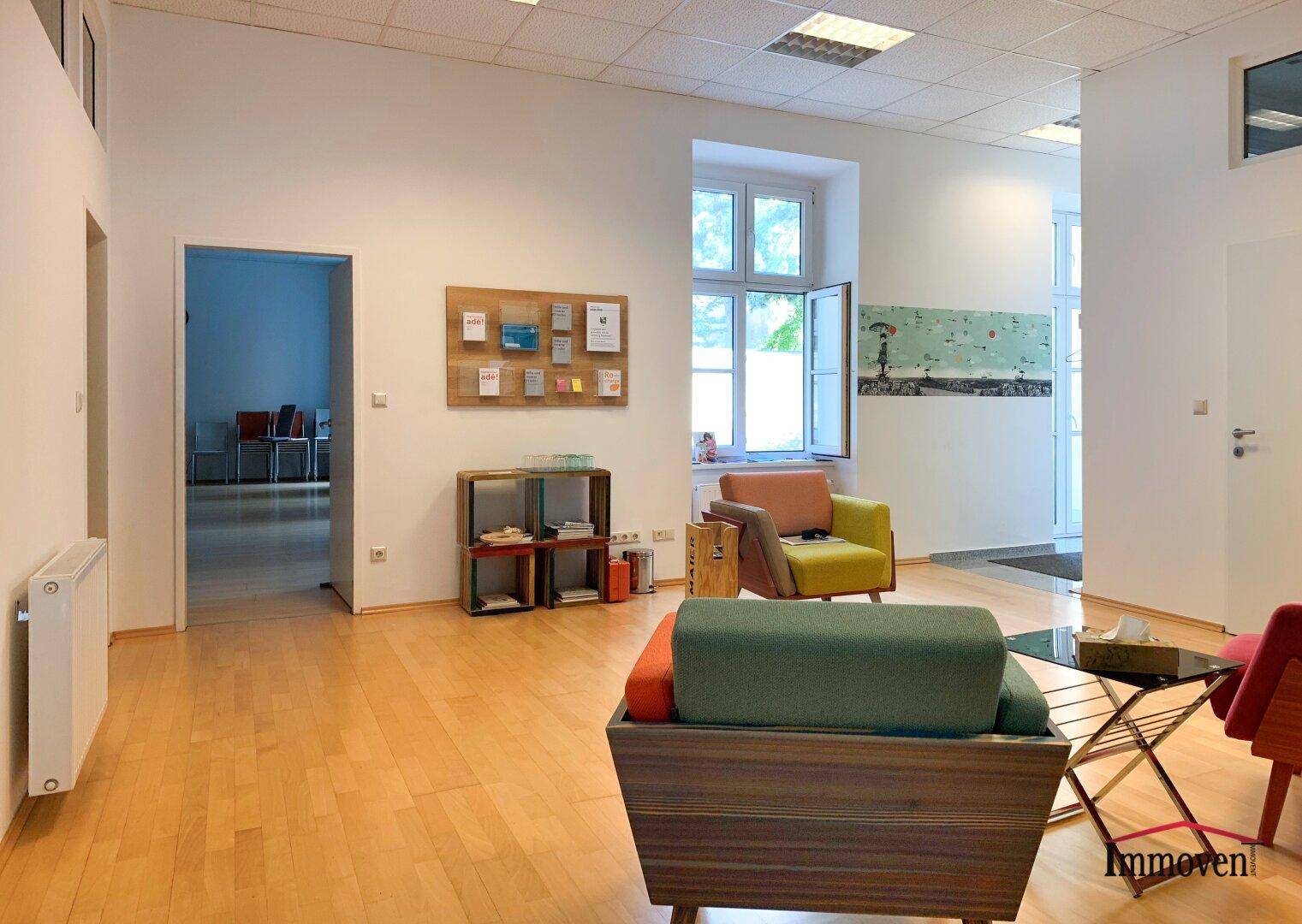 Gemütlicher Wartebereich mit modernen Sesseln, Holzboden und einem Fenster mit Blick ins Grüne.