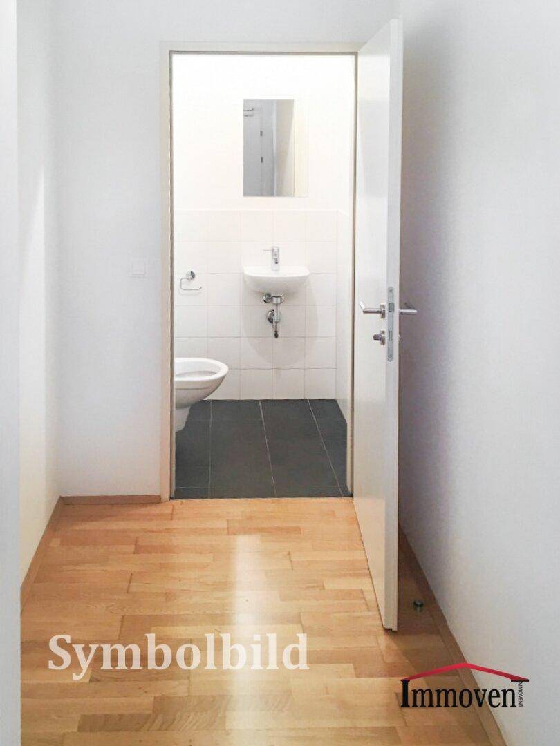 Separates WC mit Toilette und kleinem Waschbecken, ausgestattet mit dunklen Bodenfliesen.
