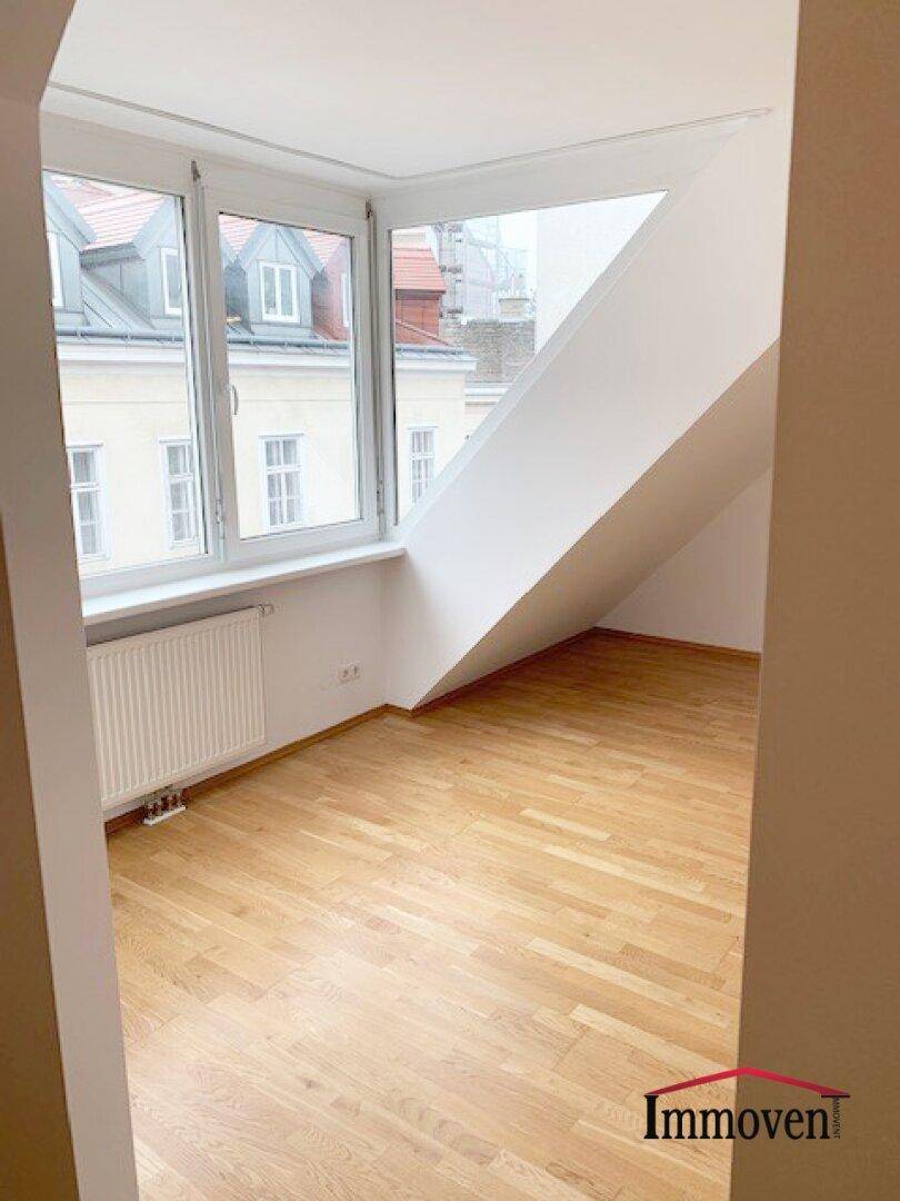 Dachgeschosszimmer mit Parkettboden, schrägen Wänden und weitem Blick über die umliegenden Gebäude.
