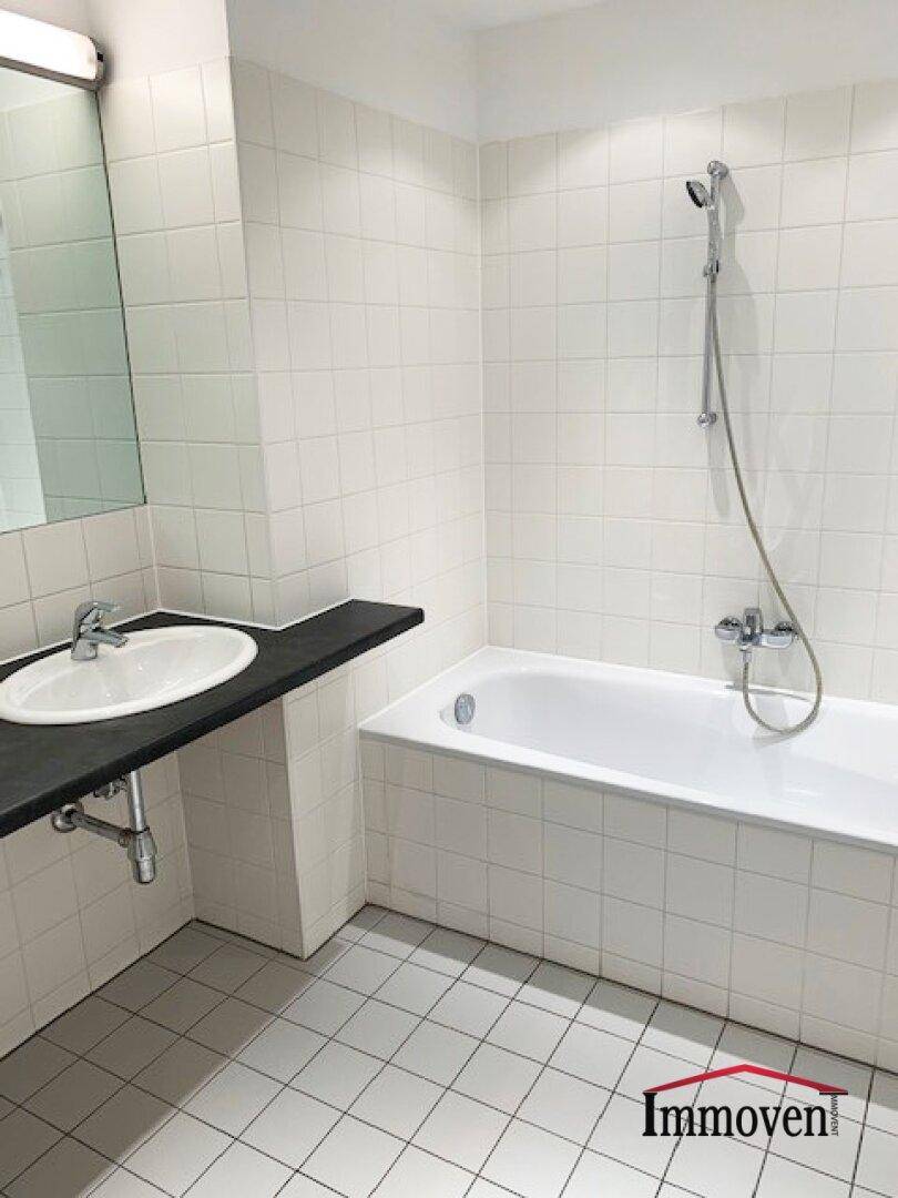 Modern gefliestes Badezimmer mit Badewanne, Duschfunktion und einem einzelnen Waschbecken.