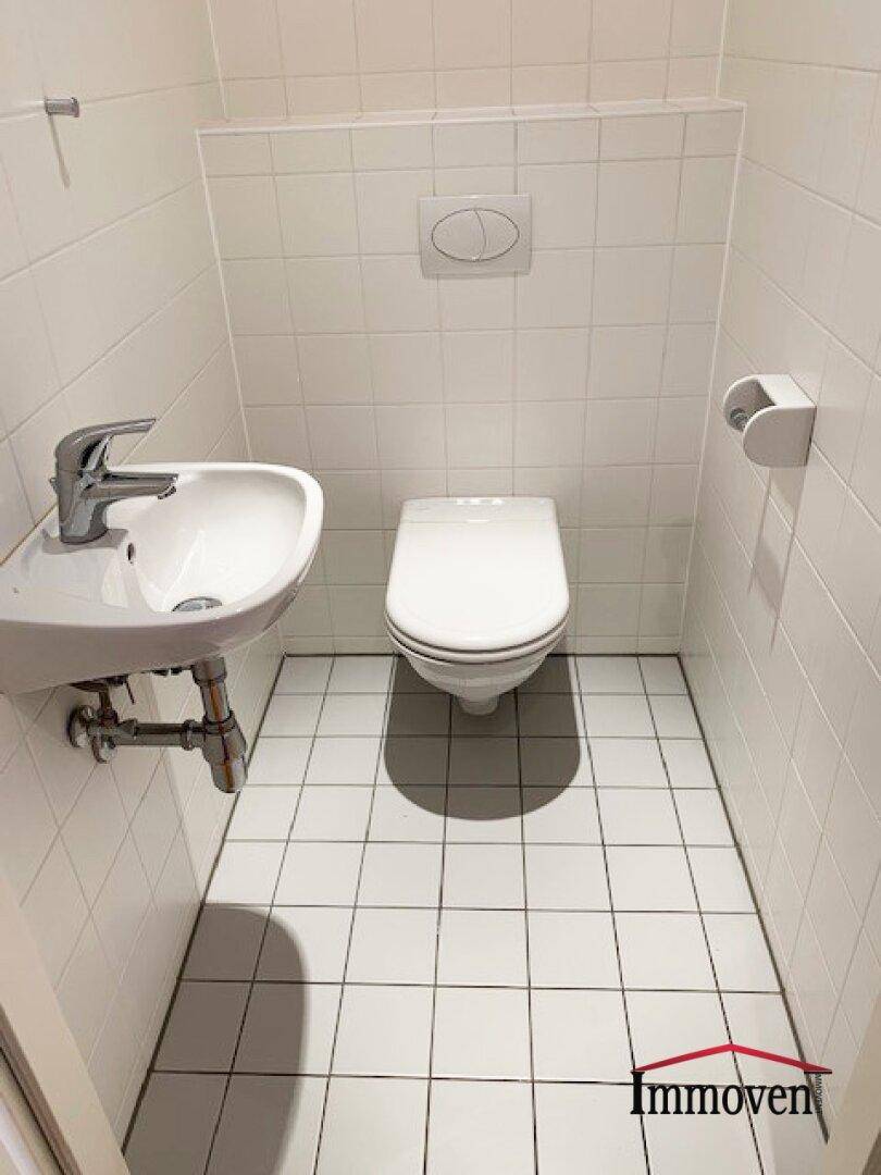 Kleines Gäste-WC mit weißen Fliesen, wandhängendem WC und einem kompakten Waschbecken.