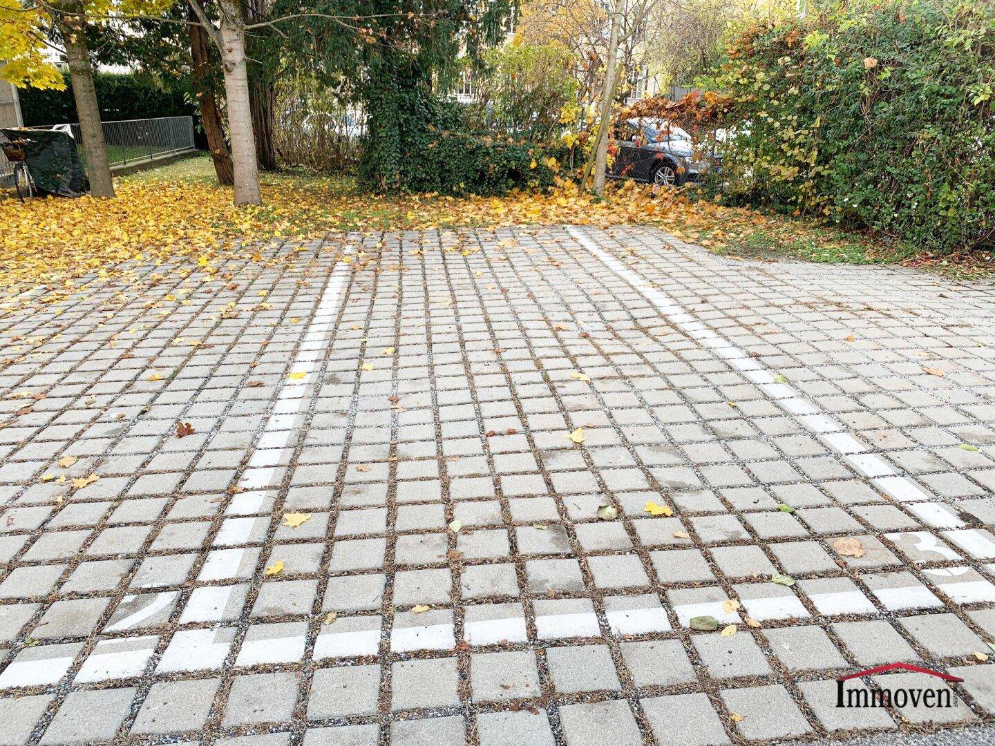 Außenparkplatz mit Rasengittersteinen und Herbstlaub, umgeben von Bäumen und Sträuchern.