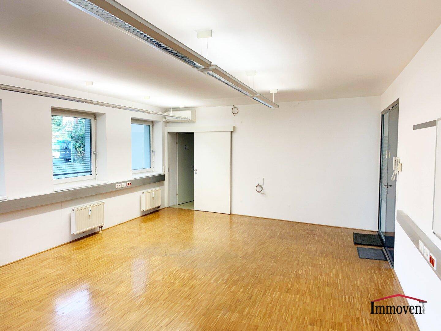 Heller Büroraum mit Parkettboden, Schiebetür und Eingangsbereich, bereit zur individuellen Gestaltung.
